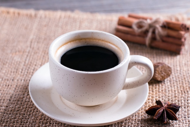 Taza de café negro en taza, anís estrellado, canela en rama sobre mesa de madera
