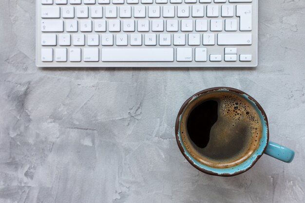 Taza de café negro y teclado de computadora en fondo rústico gris. Plano, vista superior, espacio de copia, plantilla de redes sociales, concepto de mañana e internet