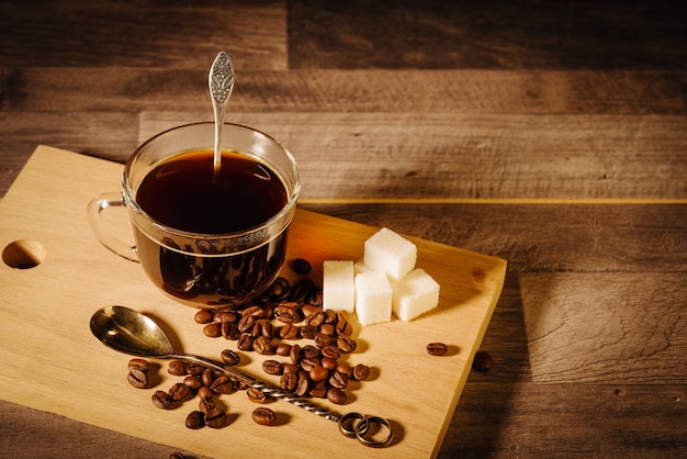 Una taza de café negro con terrones de azúcar y granos de café sobre la mesa