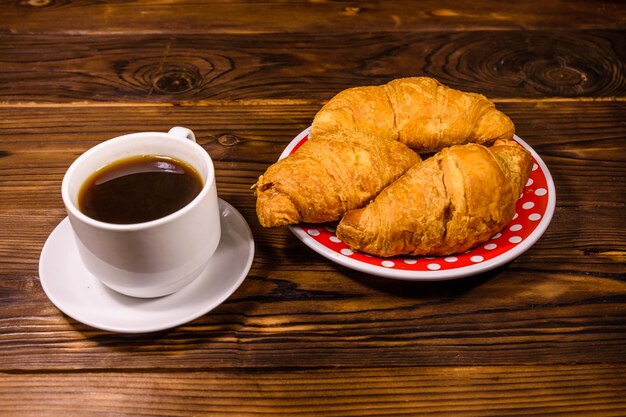 Taza de café oscuro y croissants en una mesa de madera rústica