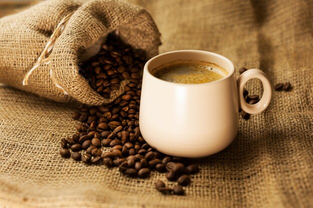 Taza de café con palitos de canela y bolsa de café en la mesa de madera