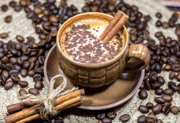 Taza de café y palitos de canela sobre un fondo de granos de café