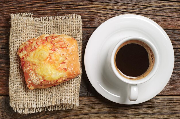 Taza de café y pan fresco con queso en la mesa de madera antigua, vista superior