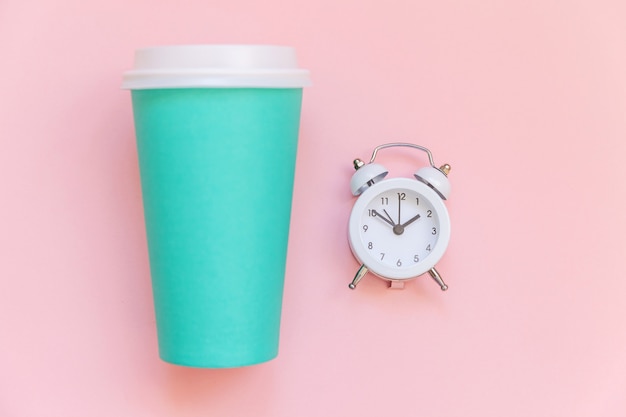 Taza de café de papel azul de diseño laico simplemente plano y reloj despertador aislado sobre fondo colorido pastel rosa