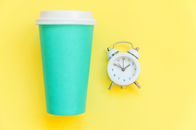 Taza de café de papel azul de diseño plano simplemente laico y reloj despertador aislado en amarillo colorido moderno