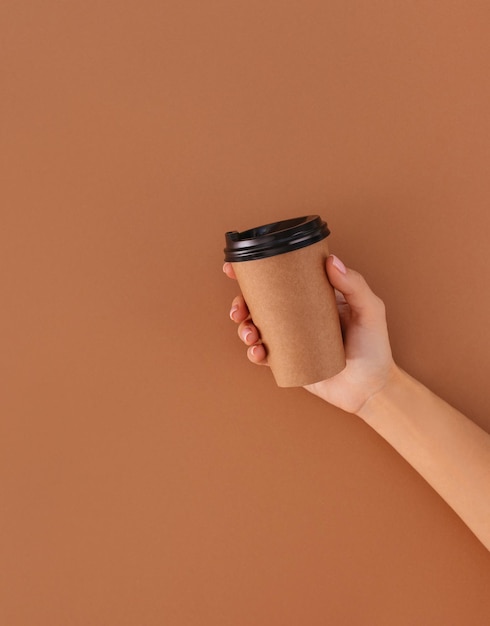 Taza de café de papel con lugar para el logotipo en la mano sobre fondo beige