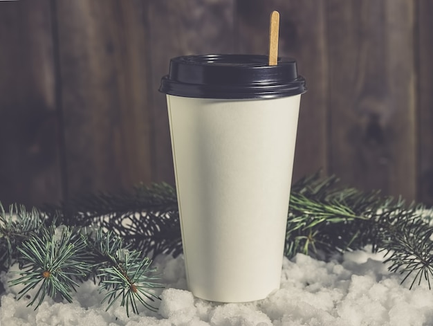 Taza de café de papel en la nieve con ramas de abeto