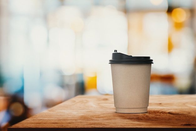 Taza de café de papel de primer plano en la mesa de madera con desenfoque abstracto cafetería interior o cafetería de fondo