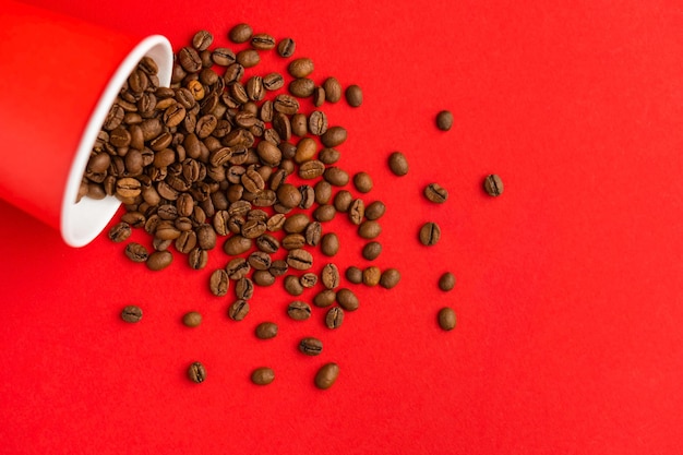 Foto taza de café de papel rojo para llevar sobre fondo rojo con frijoles tostados vertidos de ella maqueta