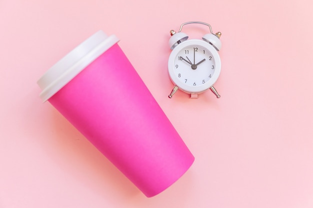 Taza de café de papel rosa de diseño plano simplemente laico y reloj despertador aislado sobre fondo colorido pastel rosa