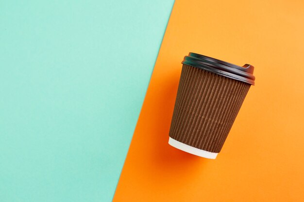 Taza de café de papel sobre superficie naranja y turquesa