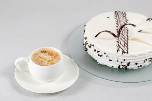 Una taza de café y un pastel blanco decorado con decoración de chocolate en un plato de vidrio sobre un fondo gris Enfoque selectivo