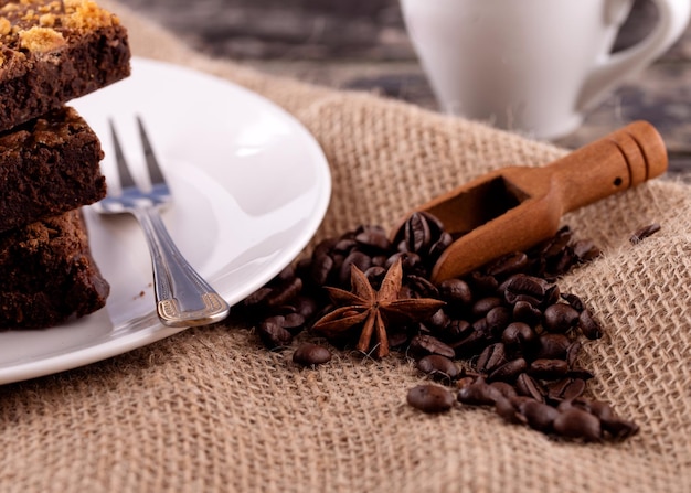 Taza de café con pastel y granos de café en un plato blanco sobre una mesa de madera en el café