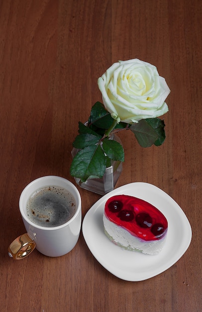 Una taza de café con un pastel y una rosa.