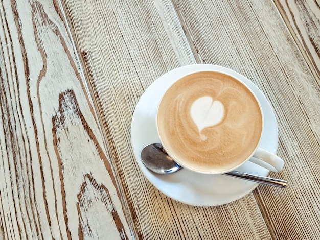 Una taza de café con patrón de corazón en una taza blanca sobre fondo de maderaCappuccino con espuma espumosa