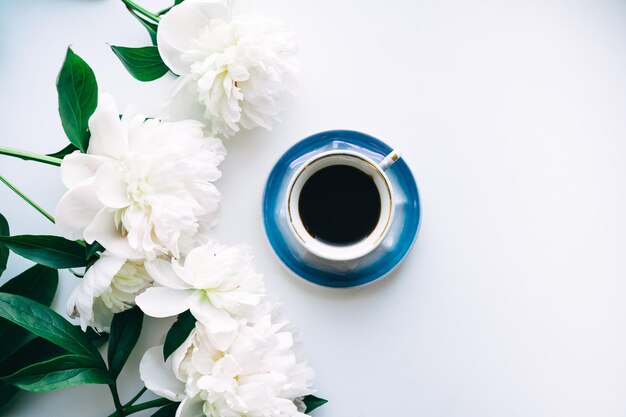 Taza de café, peonías sobre fondo blanco.