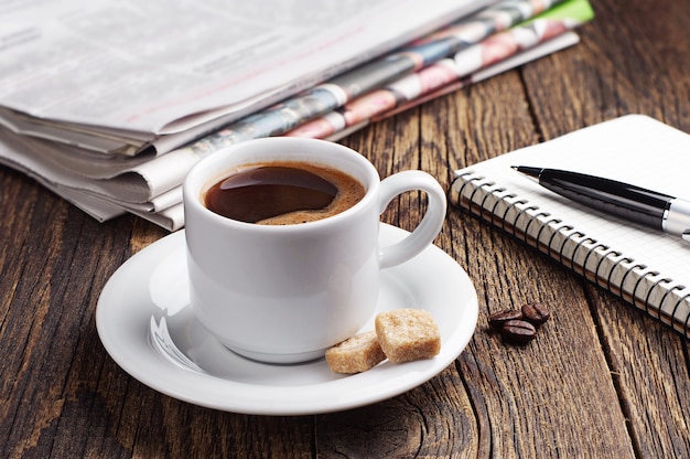 Taza de café, periódico y bloc de notas en la mesa de madera