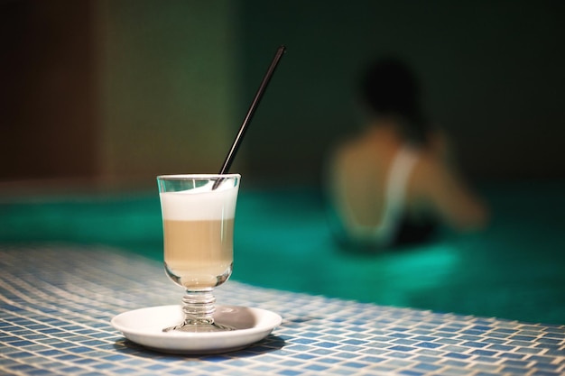 Una taza de café en la piscina y una chica al fondo.