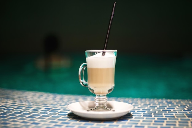 Una taza de café en la piscina y una chica al fondo.