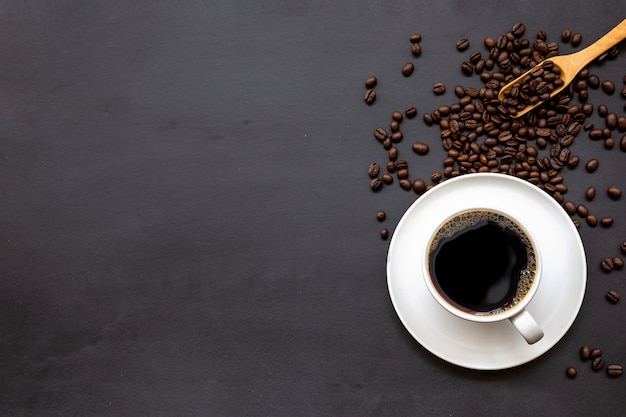 Taza de café en el piso de madera negra con granos de café y cuchara de madera