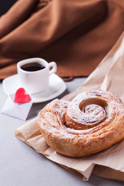 Una taza de café en un platillo y un bollo en capas