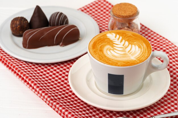 Taza de café y platillo con dulces de chocolate en la mesa de madera