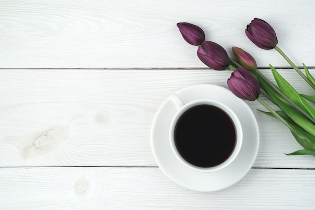 Una taza de café en un platillo y un ramo de tulipanes sobre un fondo de madera clara. Vista superior, con