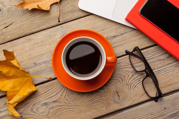 Una taza de café en el plato naranja sobre la mesa de madera. Interior de la oficina