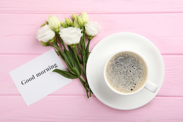 Una taza de café, un ramo de flores y una tarjeta con las palabras buenos días.