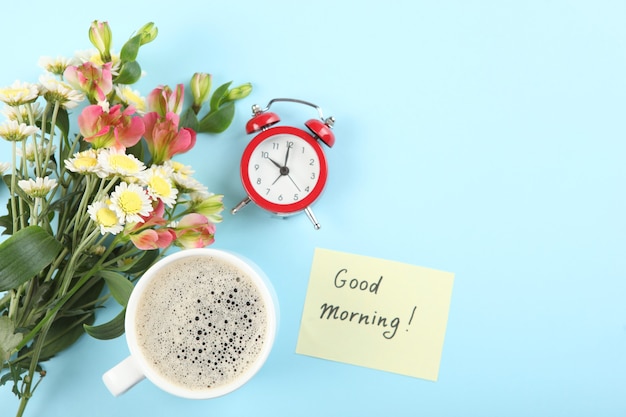 Una taza de café, un ramo de flores y una tarjeta con las palabras buenos días.