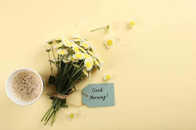 Una taza de café, un ramo de flores y una tarjeta con las palabras buenos días.