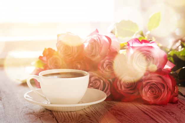 Taza de café y ramo de rosas rosadas en la mesa