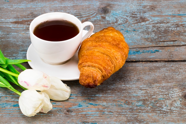 Taza de café con ramo de tulipanes y croissant en madera