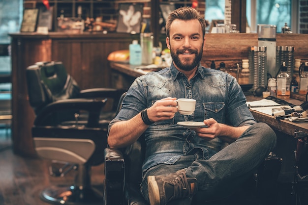 taza de café recién hecho en la barbería. alegre, joven, hombre barbudo, mirar cámara del juez