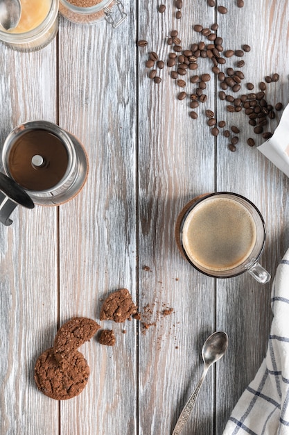 Una taza de café recién hecho con bizcochos de chocolate, granos de café tostados y olla de moka sobre una superficie de madera. Estilo parentesco. Endecha plana