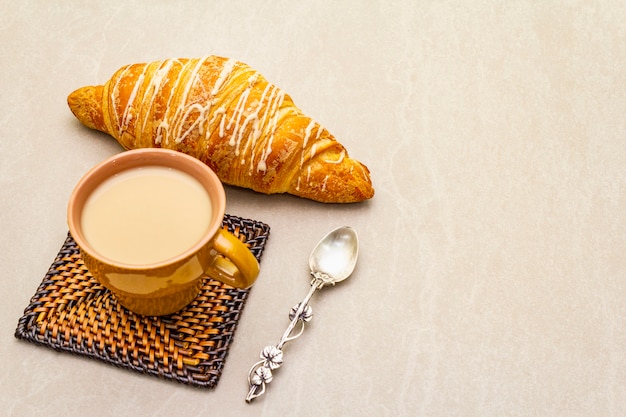 Una taza de café recién hecho con croissant. El concepto sobre una superficie de piedra con montaña rusa de mimbre y cuchara de plata vintage, copie el espacio.