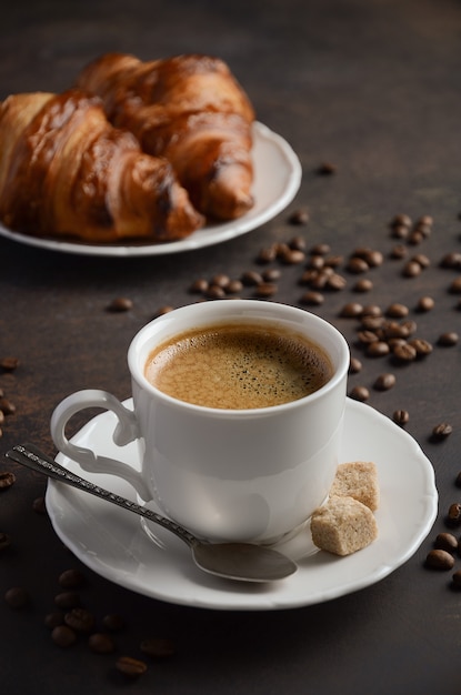 Taza de café recién hecho con cruasanes en la oscuridad.