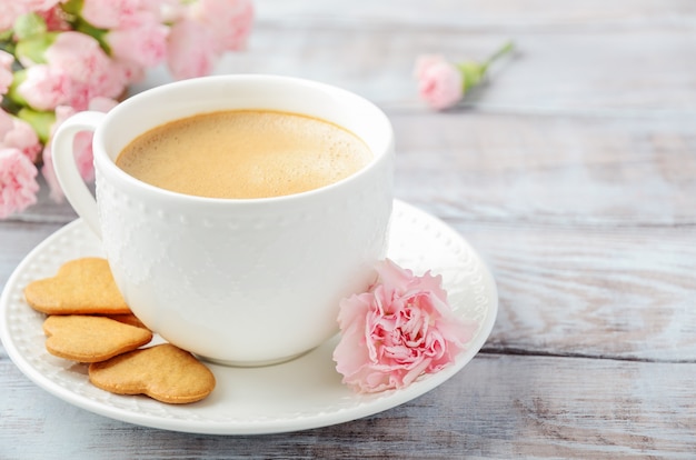 Taza de café recién hecho con flores de clavel rosa sobre una mesa de madera