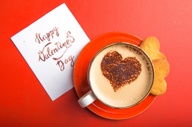 Taza de café recién hecho con galletas de corazón en la mesa roja