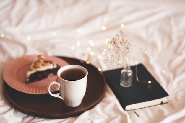 Taza de café recién hecho con sabroso pastel con flores secas en primer plano de la cama. Buenos días. Desayuno.