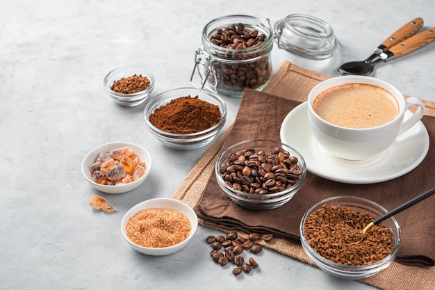 Una taza de café refrescante en una pared gris con diferentes tipos de café. Vista lateral, copie el espacio.