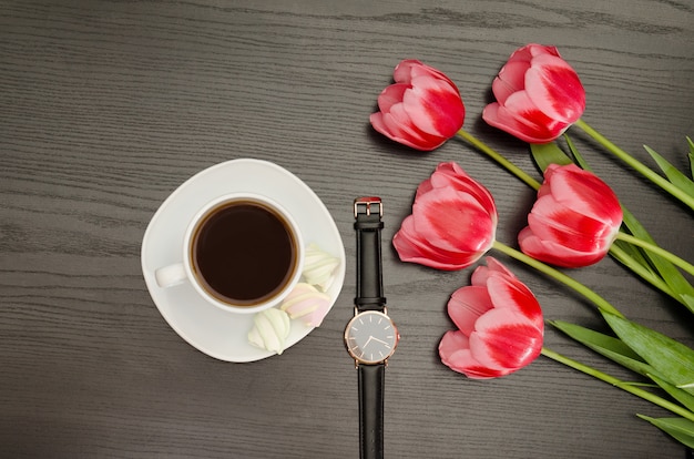 Taza con café, reloj, tulipanes rosados.