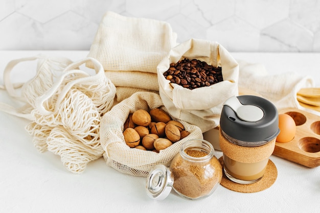 Taza de café reutilizable, produce bolsas llenas de nueces y frutos secos. Frascos de vidrio con grañones. Compras de alimentos sin desperdicio. Vida sin desperdicios
