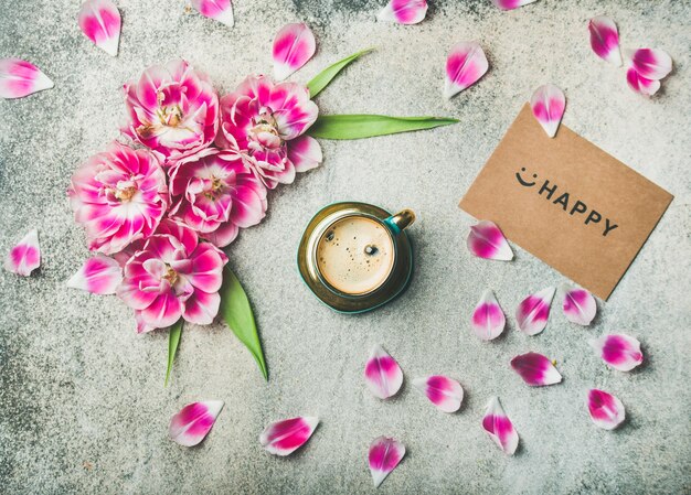 Taza de café rodeada de flores de tulipán y letrero feliz