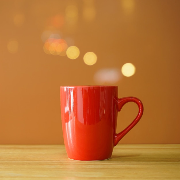 Taza de café roja en el escritorio de madera sobre fondo marrón con bokeh