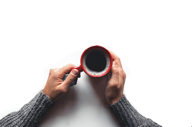 Taza de café roja en manos sobre fondo blanco.