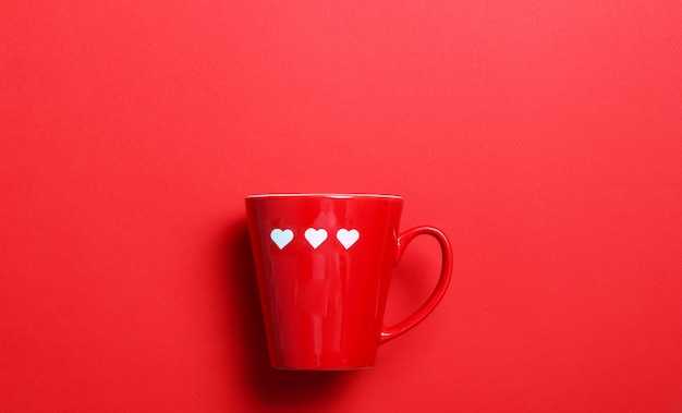 Taza de café rojo con corazones blancos en la pared roja