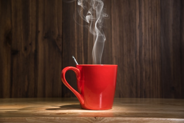 Foto taza de café rojo con humo en el fondo de la mesa de madera