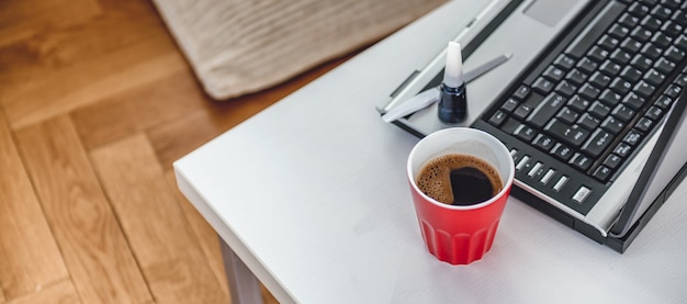 Foto taza de café rojo, pintura de uñas y fondo portátil