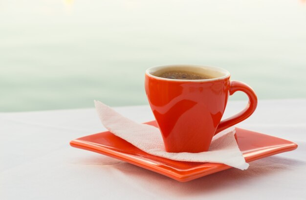 Taza de café rojo sobre la mesa con vistas al mar